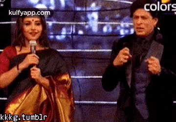 a man and a woman are standing next to each other on a stage . the woman is holding a microphone .