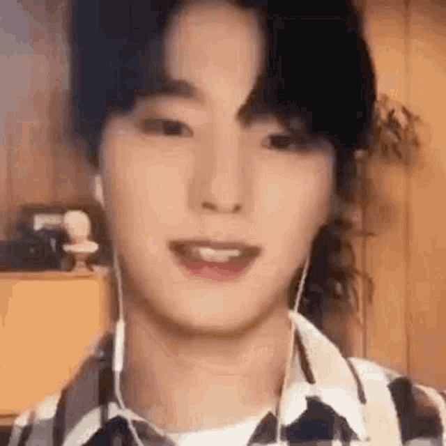 a young man wearing earphones and a plaid shirt is smiling .