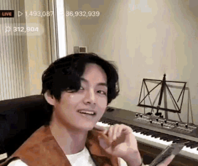 a young man is sitting in front of a piano and holding a cell phone .