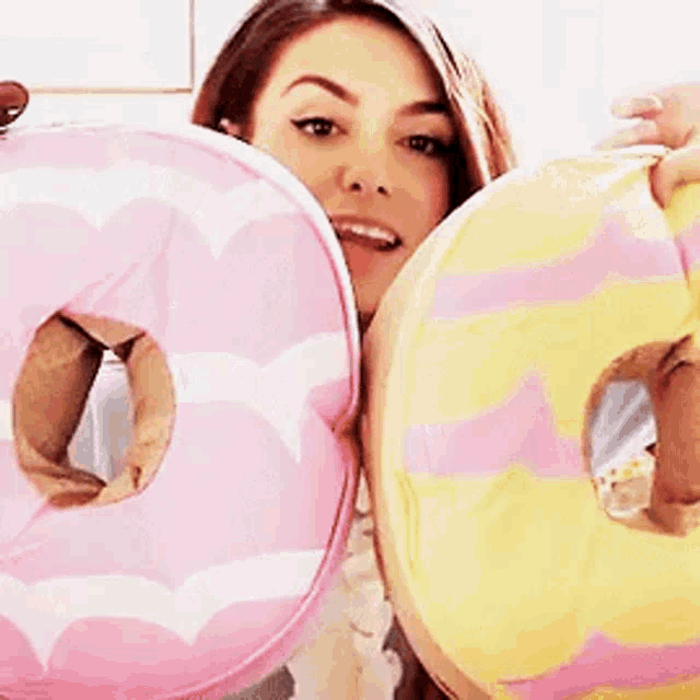 a woman is holding up two pink and yellow donuts
