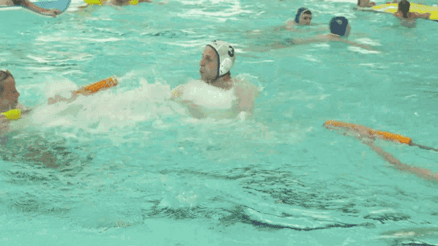a group of people are swimming in a pool and one of them is wearing a white helmet