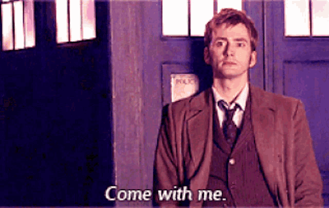 a man in a suit and tie is standing in front of a blue door and saying come with me