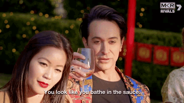 a man holds a glass of wine while a woman looks on and says you look like you bathe in the sauce