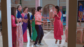 a group of people are dancing in a room with a woman in a pink dress .