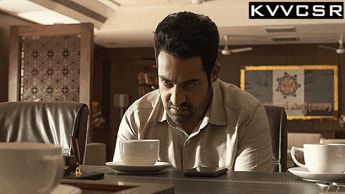 a man sits at a desk with a cup of coffee and a cell phone with a kvvcsr logo in the background