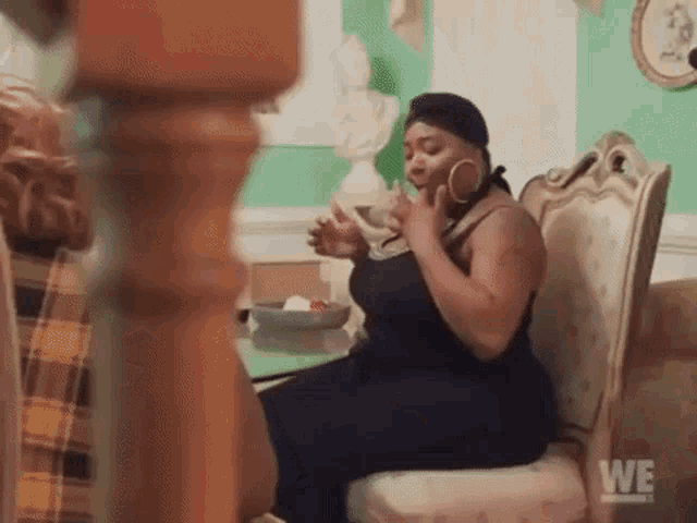 a woman is sitting in a chair talking on a cell phone while drinking from a glass .