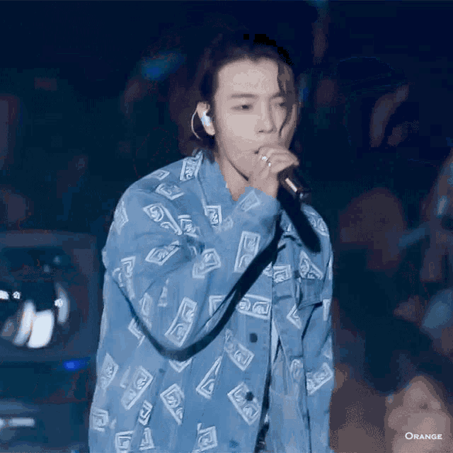 a man in a blue jacket is singing into a microphone while wearing headphones .