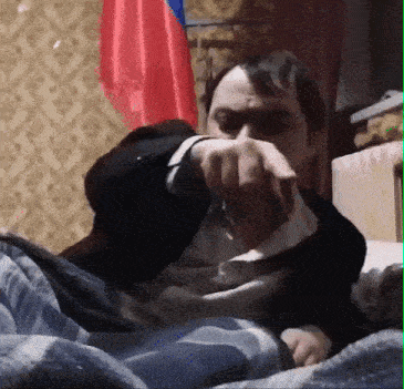 a man is laying on a bed with a blanket and a flag behind him .
