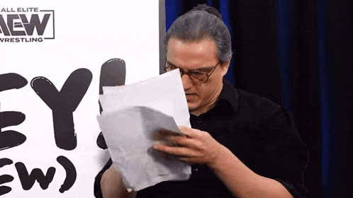 a man reads a piece of paper in front of a sign that says all elite wrestling