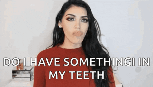 a woman in a red sweater is making a funny face and saying do i have something in my teeth