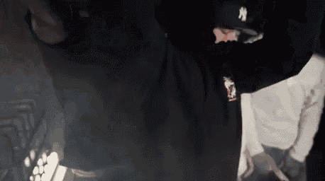 a man in a black hat is standing in a dark room with his arms outstretched .