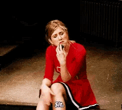 a woman in a red dress is sitting on the ground talking on a cell phone and says sit .