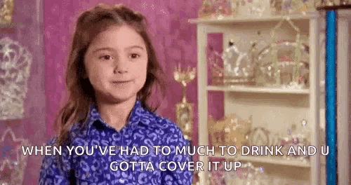 a little girl in a blue shirt is standing in front of a shelf full of trophies .