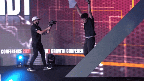 a man holds up a piece of paper in front of a banner that says conference 2021