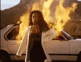 a woman is standing in front of a white car that is on fire