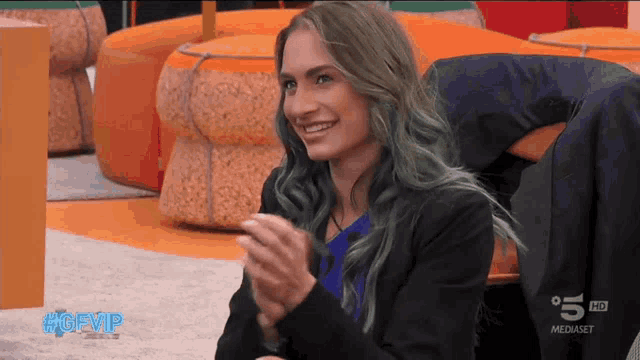 a woman with blue hair is smiling and clapping in front of a tv screen that says 5 hd