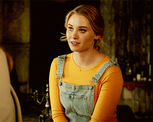 a woman wearing overalls and a yellow top smiles