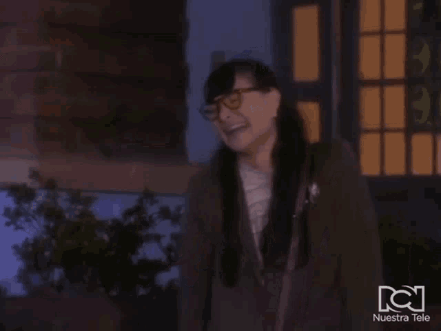 a woman wearing glasses is waving in front of a nuestra tele ad