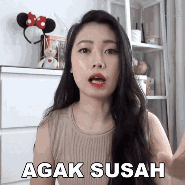 a woman wearing a headband with minnie mouse ears says agak susah