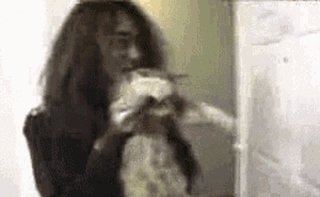 a woman with long hair is holding a cat in her arms in front of a refrigerator .