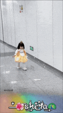 a little girl in a yellow dress is standing next to a trash can with the name sheita written on it