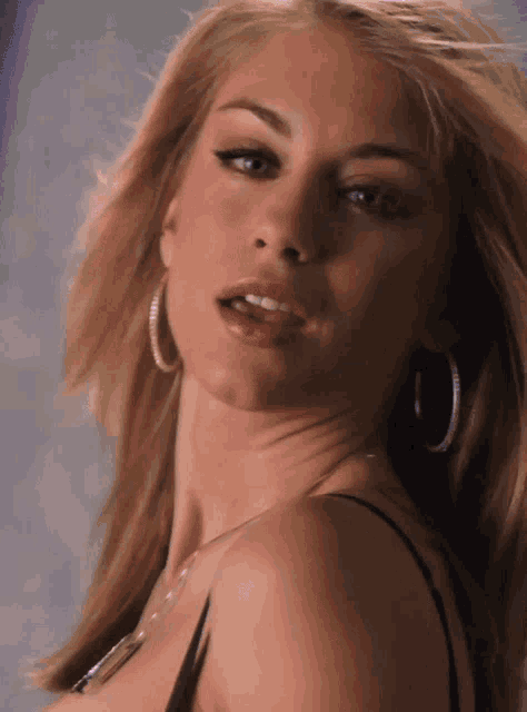 a woman wearing hoop earrings and a black top looks at the camera