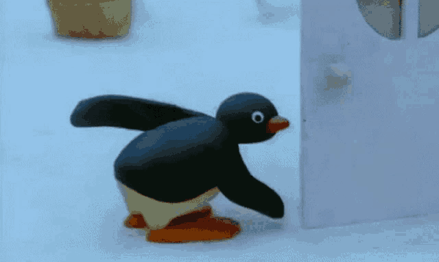a cartoon penguin is standing next to a white wall .