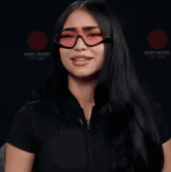 a woman wearing glasses and a black shirt is smiling and clapping
