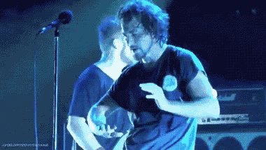 a man with a beard is dancing on a stage in front of a microphone while another man stands behind him .