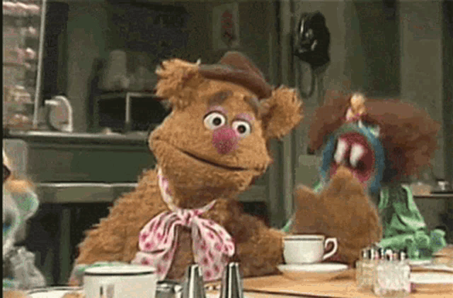 two stuffed animals are sitting at a table with a cup of coffee and salt and pepper shakers