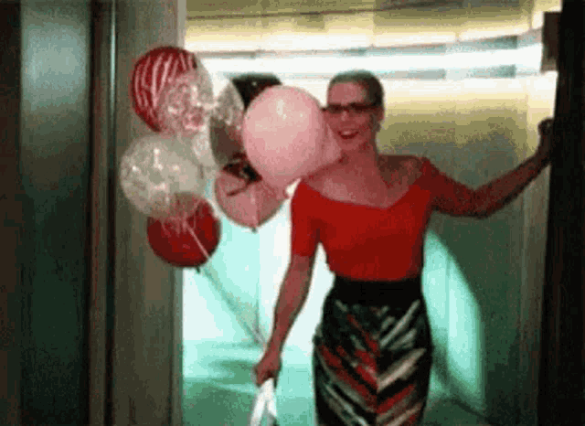 a woman in a red top is holding a bunch of balloons .