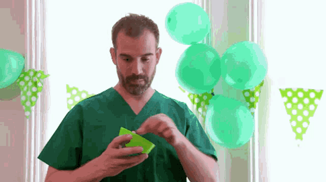 a man in a green scrub is holding a green box in front of balloons