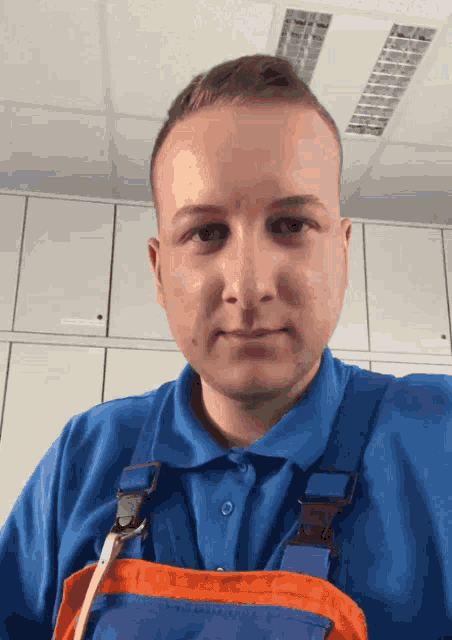 a man wearing a blue shirt and orange overalls is looking at the camera