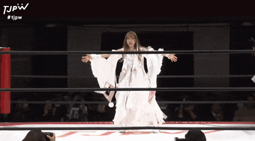 a woman in a white dress stands in a wrestling ring with tjpw written on the bottom right