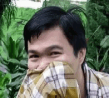 a man in a plaid shirt is smiling and covering his face with his shirt .