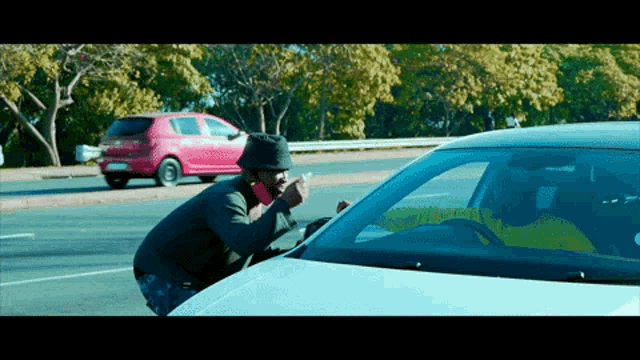 a man smoking a cigarette next to a car with a sticker on the windshield that says ' a '