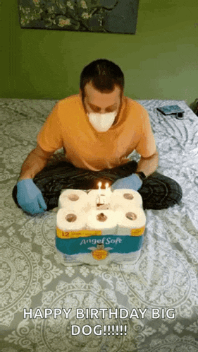 a man wearing a mask and gloves is sitting on a bed surrounded by rolls of toilet paper .