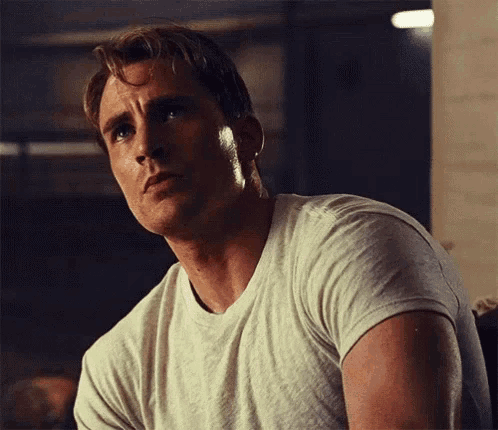 a close up of a man wearing a white t-shirt looking at the camera .