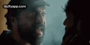 a man with a beard is sticking his tongue out at another man in a dark room .