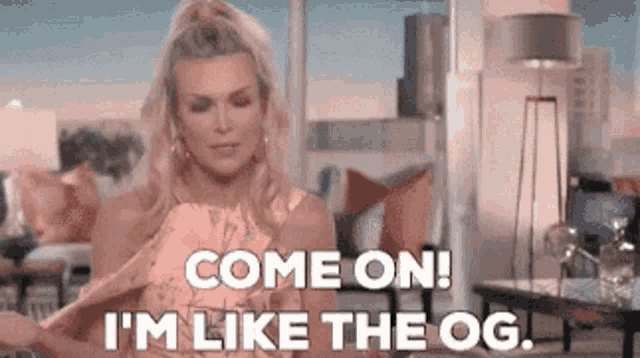 a woman in a pink dress is standing in a living room and saying come on i 'm like the og
