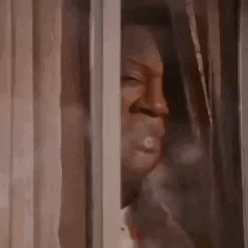 a woman is peeking out of a window with her eyes closed and smiling .