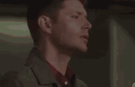 a man in a trench coat and a red shirt is standing in a dark room and looking up .