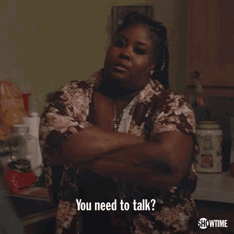 a woman in a floral shirt is sitting at a table with her arms crossed .