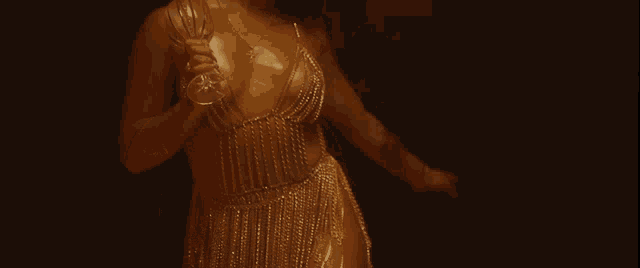 a woman in a gold dress holds a glass in her hand