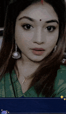 a woman with a red dot on her forehead is wearing earrings and a green shirt