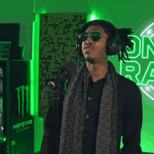 a man wearing headphones is singing into a microphone with a monster energy sign in the background