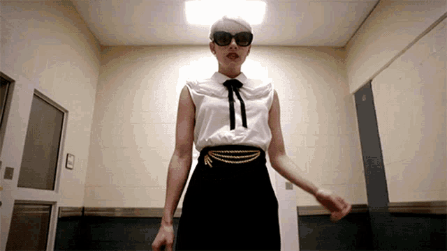 a woman wearing sunglasses and a white shirt is standing in a room