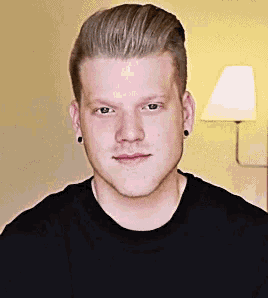 a young man wearing a black shirt and ear piercings looks at the camera