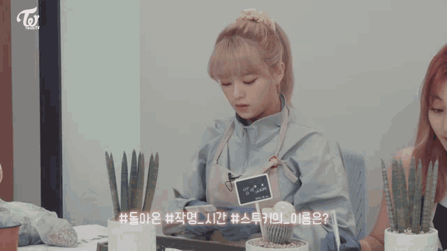 two girls are sitting at a table with potted plants and one has a name tag that says twice