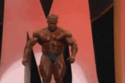 a bodybuilder in a blue bikini is standing on a stage in front of a red curtain .